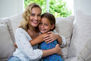 Portrait of mother and daughter embracing on sofa