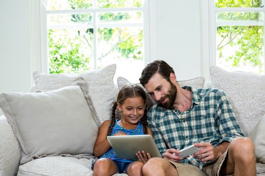 Happy girl showing digital tablet to father on sofa