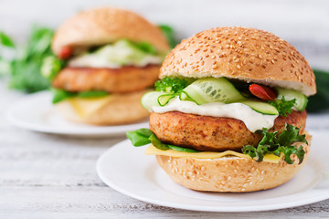 Big sandwich - hamburger with juicy chicken burger, cheese, cucumber, chili and tartar sauce on a light wooden background