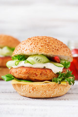 Big sandwich - hamburger with juicy chicken burger, cheese, cucumber, chili and tartar sauce on a light wooden background