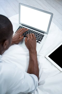Young man lying on bed and using laptop