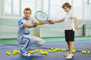 Instructor or coach teaching child how to play tennis on a court indoor