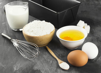 Ingredients for pastries: flour, eggs, milk against a dark backg