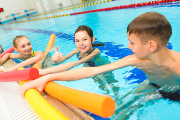 Happy and smiling group of children learning to swim with pool noodle