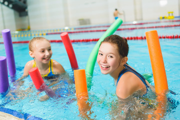 Happy and smiling group of children learning to swim with pool noodle