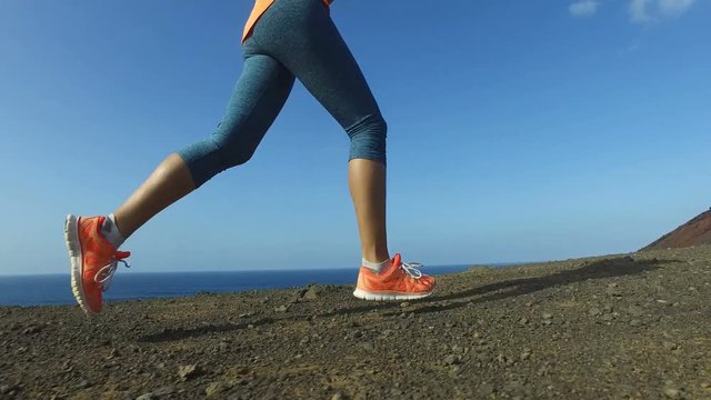 Running woman outdoors on run. Fast female runner running shoes and legs close up on mountain trail.  Female is in sportswear. Fitness woman exercising in nature on sunny day.  ACTION CAMERA.