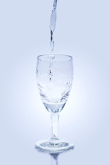 Pouring water into wine glass on blue background