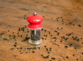 Still life with black peppercorn and manual mill with red cap, standing on wooden background....
