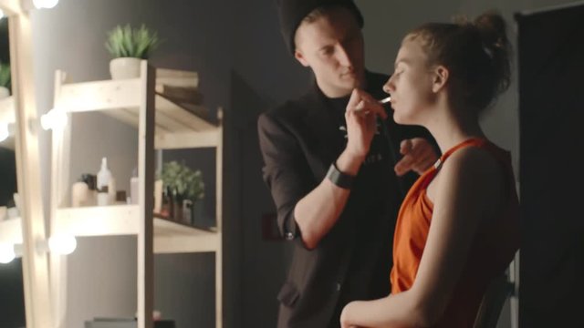 Male makeup artist applying foundation on face of model with brush, zooming in 