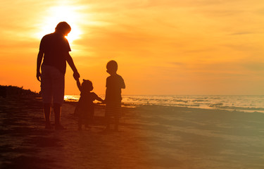 father and two kids walking on beach at sunset