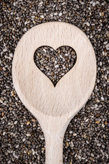 Cooking wooden spoon with heart shape cutted on chia seeds background.