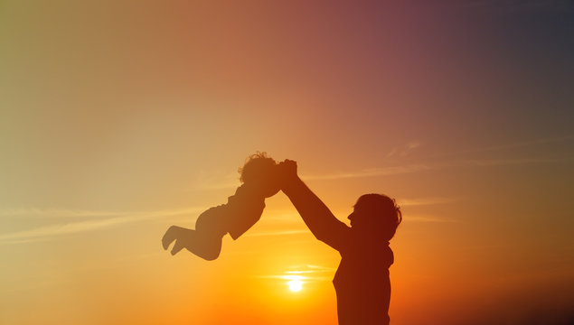 Father and little daughter play silhouettes at sunset