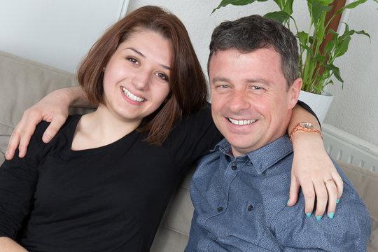Couple smiling at the camera at home in living room