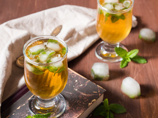 Cold tea with ice and mint leaves on dark wooden table with a book and ice cubes