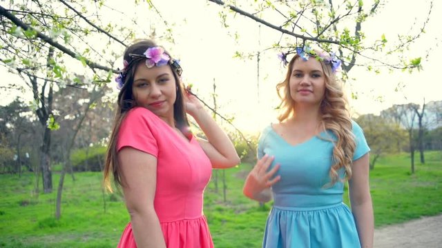 two girls wearing circlets of flowers posing in spring blossom park slow motion