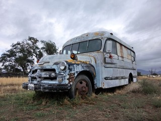 Abandoned old vintage rusty white metal bus in overgrown field - landscape color photo