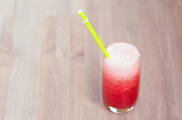 A watermelon smoothie in a glass with tube on a wooden background