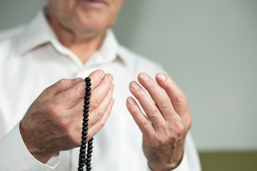 Praying hands of an old man holding rosary beads. Selective focus