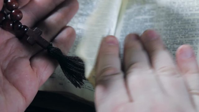 human hands holding the Bible and praying with a rosary