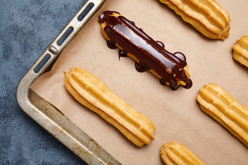 Eclairs or profiteroles with chocolate and whipped cream preparing on baking sheet background. Traditional homemade French cuisine dessert. Top view