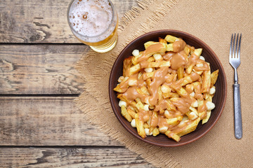 Poutine traditional Canadian meal with fries, curd cheese, beer and sauce on vintage wooden table background. Rustic style.