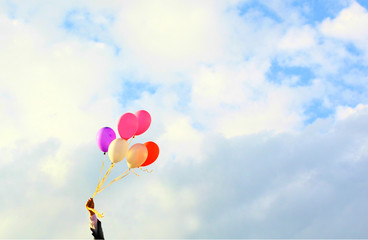 The hand holding colorful balloons with blue sky background, concept of love in summer and valentine, wedding. Selective focus on the balloons