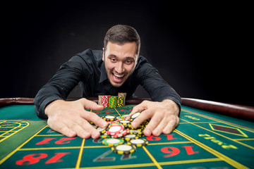 Young handsome man playing roulette wins at the casino