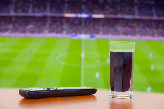 Coke fizzy drink, tv remote on a table. Watching football (socce