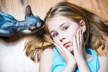 Beautiful girl with gray sphinx cat lying on flour in room