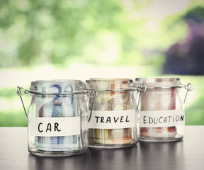 Three jars for different needs full of banknotes on nature background