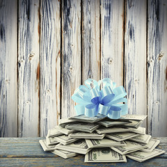 Pile of dollars with bow as gift on wooden background