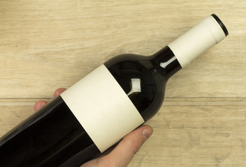 Young man's hand is holding red wine bottle at the light wooden background closeup