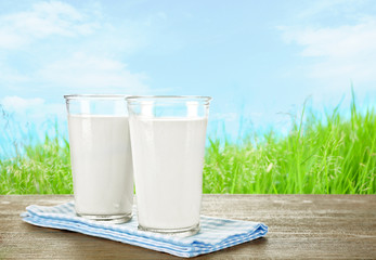 Glasses of milk on wooden table against grass and blue sky background