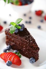 Chocolate cake with chocolate cream and fresh berries on plate, on light background