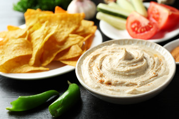 Ceramic bowl of tasty hummus with chips on table
