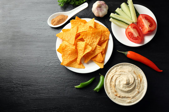 Ceramic bowl of tasty hummus with chips and chili on table