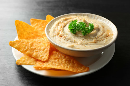 Ceramic bowl of tasty hummus with chips and parsley on table