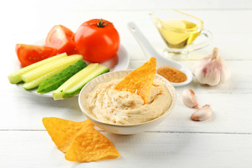 Ceramic bowl of tasty hummus with chips, oil and vegetables on table