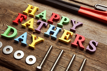 Happy Father's Day inscription with work tools on wooden background. Greetings and presents