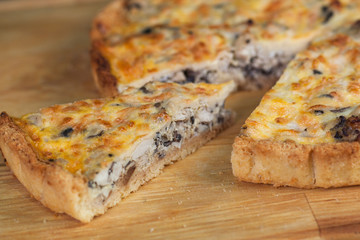 pie with chicken, mushrooms, cheese and eggs, with cut pieces on a wooden board