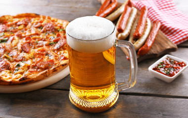 Grilled sausages, delicious pizza and glass of beer on wooden table, close up