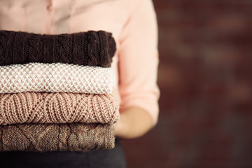 Stack of knitted clothes in female hands on blurred wall background