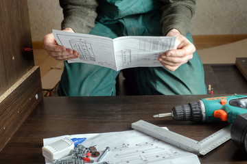 Frustrated man reading instruction and putting together furniture