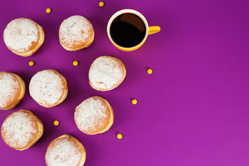 Delicious donuts with powdered sugar and cup of coffee on purple surface, top view