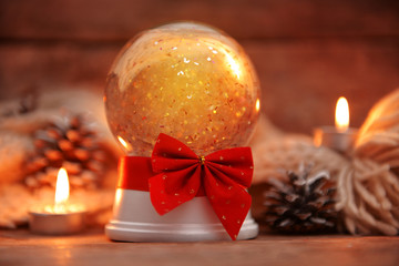 Christmas snow globe with ribbon bow in candlelight on wooden table closeup