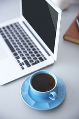 Modern interior. Comfortable workplace. Table with laptop and cup of coffee on it, close up