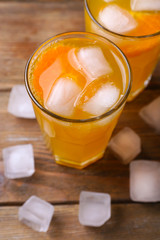 Glasses of orange juice with ice block on wooden background, close up