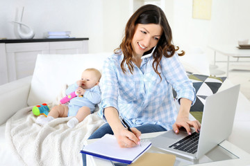Beautiful woman with baby boy working from home using laptop