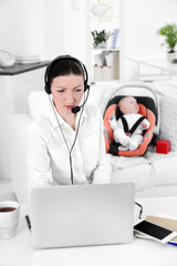 Businesswoman with baby boy working from home using laptop and headset