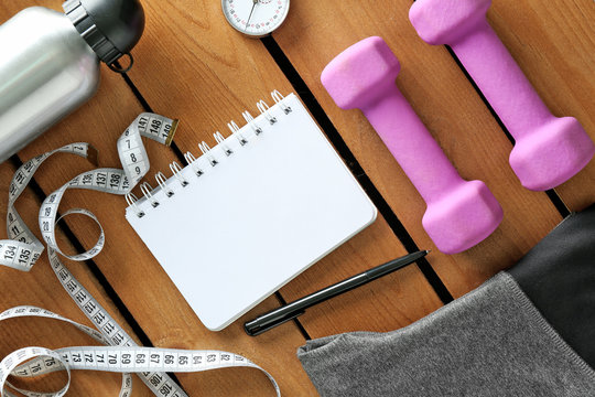 Athlete's set with female clothing, equipment, bottle of water and notebook on wooden background